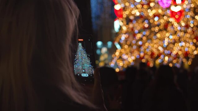 Close-up female hands holding smartphone recording video on smartphone camera with raised hands near stage. Crowd at christmas concert Young people having fun on New Year Eve town square music show.