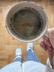 female hand holds cup of coffee with heart shape on foam