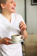 Happy lovely young female health worker laughing sincerely while holding cup of hot tea