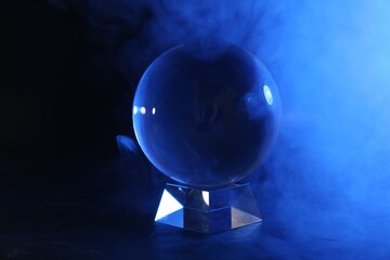 Magic crystal ball on table and smoke against dark background. Making predictions