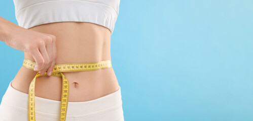 Slim woman measuring waist with tape on light blue background, closeup and space for text. Weight...