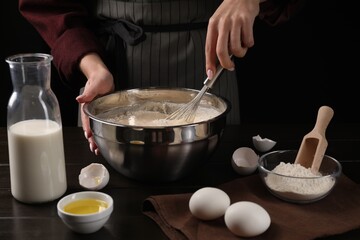Woman making dough with whisk in bowl at table, closeup