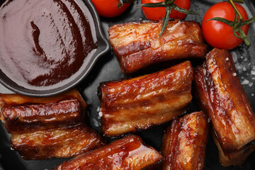 Tasty roasted pork ribs with sauce and tomatoes on plate, flat lay