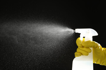 Woman spraying liquid from bottle on black background, closeup