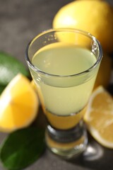 Tasty limoncello liqueur, lemons and green leaves on table, closeup