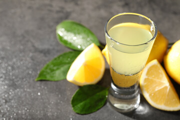 Tasty limoncello liqueur, lemons and green leaves on grey table, closeup. Space for text