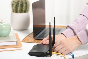 Woman connecting cable to Wi-Fi router at table indoors, closeup