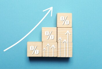 Mortgage rate rising illustrated by upward arrows and wooden cubes with percent signs on light blue...