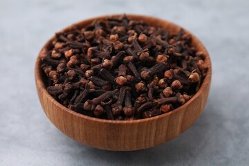 Aromatic cloves in bowl on gray table, closeup