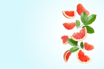 Fresh grapefruit pieces and green leaves falling on light blue background. Space for text