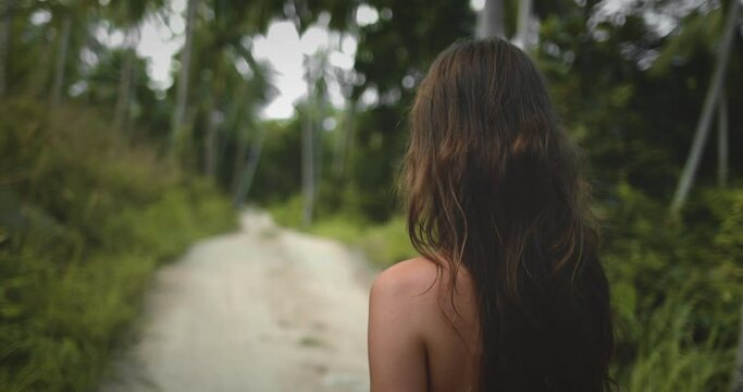Female hiking jungle pam tree forest trail close up. Beautiful long hair caucasian girl explore exotic island nature, relax, enjoy outdoor lifestyle travel on summer holiday vacation. Asia. Back view