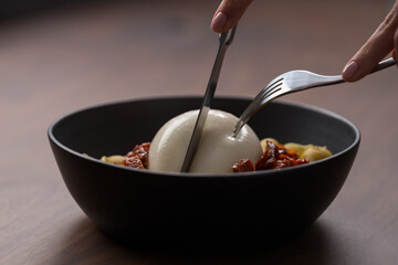 Closeup of pesto conchiglie with sundried tomatoes and cutting burrata cheese served in black bowl - obrazy, fototapety, plakaty