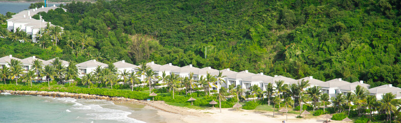 Panorama view white sandy beach with row houses, luxury vacation homes, ocean view villas surrounding by coconut palm trees, mountain, lush green tropical forest background Hon Tre, Nha Trang