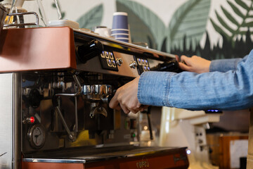 Unrecognizable hands of Asian barista female making hot coffee from professional machine standing behind cafe shop counter bar, young waitress worker wearing apron working in cozy small restaurant