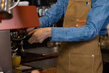 Unrecognizable hands of Asian barista female making hot coffee from professional machine standing behind cafe shop counter bar, young waitress worker wearing apron working in cozy small restaurant