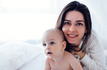 Pretty infant in a white bodysuit with his mom on a light background. Motherhood concept.