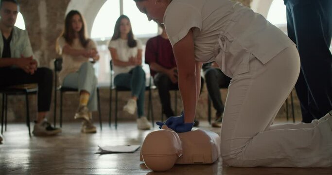 Close-up shooting: A female doctor in white uniform conducts practical medical training by pressing her hands on the breast of a medical mannequin for the public, who listens to her