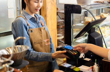 Closeup waitress hand holding credit card swipe on wireless digital payment machine, worker wearing...