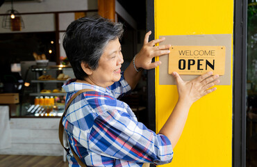 Asian 60s healthy senior barista worker female holding opening sign board pose in front of bakery shop retail small business owner start-up routine working, happy elderly retired pensioner lifestyle