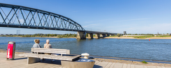 Two woman sitting on bench enjoying the view from the river quay called Waalkade in Nijmegen The...