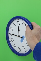 Wall clock held by man's hand on green screen background.