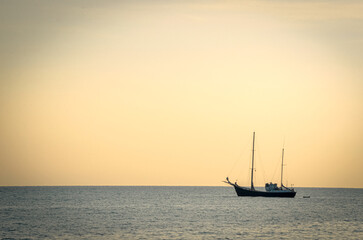 Fototapeta premium Yacht resting on sea water in sunset light with a tiny still visible plane rising from the nice airport