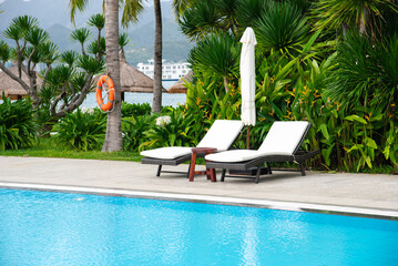 Beachside swimming pool at upscale resort with safety life buoy, lounger chairs white cushion,...