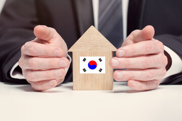 Businessman hand holding wooden home model with Korean flag. insurance and property concepts