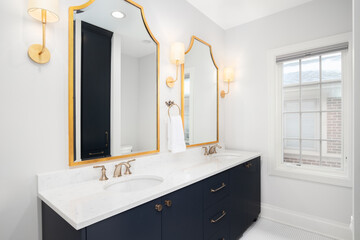 A bathroom with a blue cabinet, white marble countertop, and gold light fixtures and mirrors.