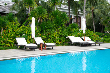 Coconut palm trees and tropical garden surrounding swimming pool at upscale resort with row of...