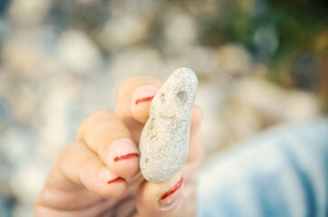 Woman with manicure holding a sea stone in fingers in bright sun light with strong bokeh