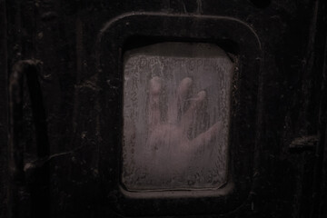 A girl's palm behind a dirty window in an abandoned bunker. A shabby rusty door. Dirty glass.	
