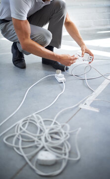 Hands, man and electrician plug connection, power and electricity in office. Cord, wire and cable on floor, socket and energy of worker, professional or employee charging on technology in workplace