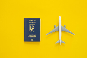 Ukrainian biometric passport, dollar bills and airplane figurine on a yellow background, top view....