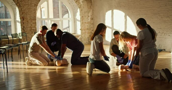 A professional doctor Black man in a blue medical uniform, together with a nurse girl in a white medical uniform, conduct first aid training using various mannequins. A group of learners practice