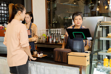Asian waitress barista worker accepts credit card cashless payments from customer female in cafe restaurant, happy woman open bakery coffee shop, small business entrepreneur start-up lifestyle