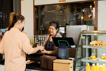 Asian waitress barista worker accepts credit card cashless payments from customer female in cafe...