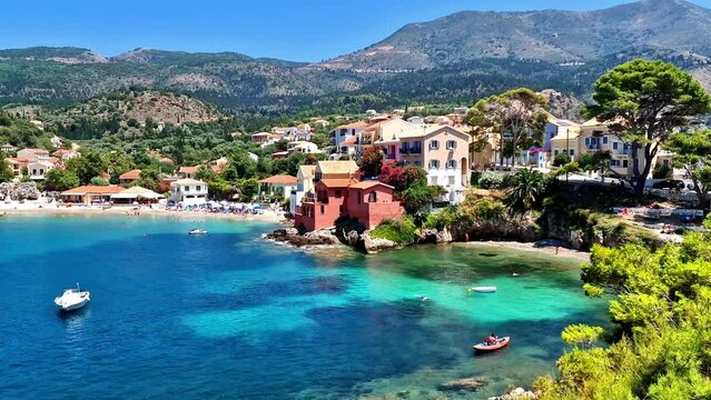 Assos village beach Kefalonia Greece 4K. Panoramic view of turquoise bay and colorful traditional houses surrounded by green pine trees with boats in Ionian Sea. Scenic travel b roll stock video
