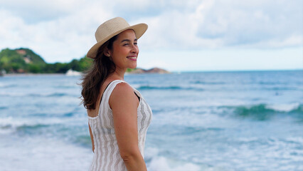 Fototapeta premium Happy young white woman wearing hat feeling the sea breeze. Beautiful smiling girl relaxing and enjoy the sun at seaside. 