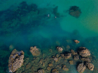 Fototapeta na wymiar Two snorkelers swimming in turquoise sea near the rocks in Malta aerial top down. Perfect summer holidays activity.