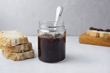 Strawberry jam in a glass jar on a light gray background with sliced ​​bread. Composition with delicious homemade jam. Breakfast and snack concept.