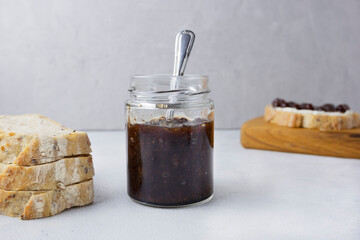 Strawberry jam in a glass jar on a light gray background with sliced ​​bread. Composition with delicious homemade jam. Breakfast and snack concept.