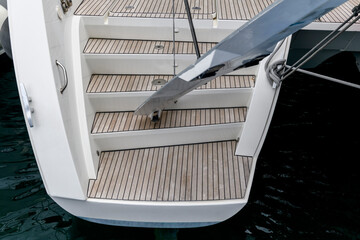 Stern of super luxury yacht berthed in marina. Teak deck on stern of sailing boat. Teak stairs...