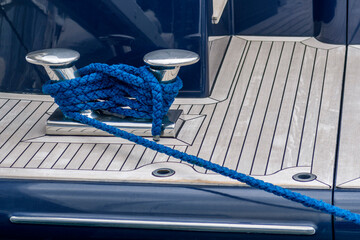 Stainless steel cleat with blue rope on a superyacht deck. Mooring line wrapped around bitts on...