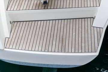 Stern of super luxury yacht berthed in marina. Teak deck on stern of sailing boat. Teak stairs...