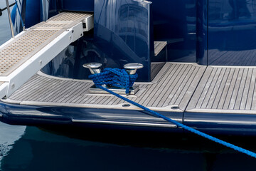 Stainless steel cleat with blue rope on a superyacht deck. Mooring line wrapped around bitts on...