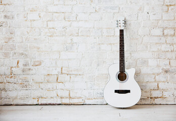 Acoustic white guitar leaning against a white wall in an empty room