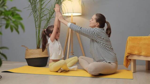 Fitness joy for kids. Wellness moments daily. Family exercise happiness. Mom guides workouts. Young trainer and her little female child doing physical workout together at home