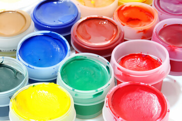 children's hobby. bright colored gouache paints in small transparent jars close-up top view, artistic concept