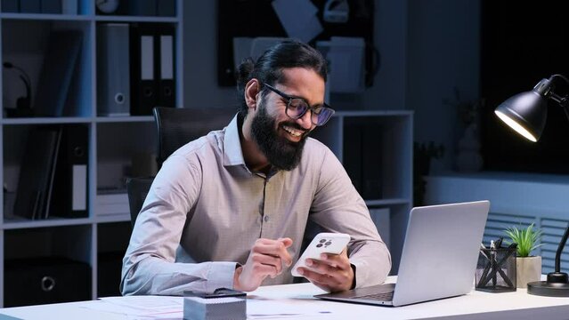 Businessman is captured using phone and sharing a laugh during a break. Attired in professional attire, relaxed expressions convey a moment of respite in the late hours.